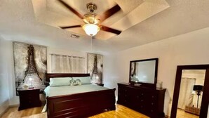 A bedroom with a wooden floor, a bed with a headboard, a ceiling fan, a TV on a dresser, and artwork on the walls. - Casa Santa Clara with Swimming Pool near Golf Country Clubs (Brownsville)