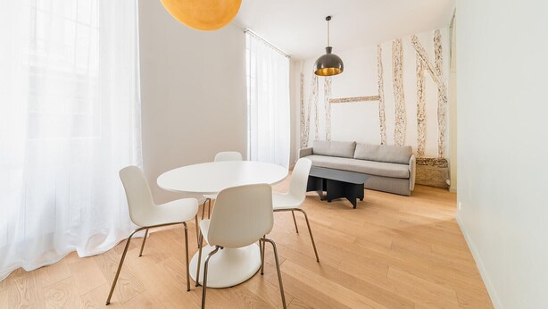 A modern dining area with a round table and white chairs, a grey sofa, and a hanging pendant light.