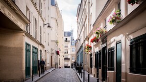A narrow cobblestone street flanked by historic buildings with green shutters and flower boxes.