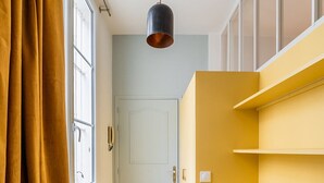 A narrow hallway with a wooden floor, a door at the end, and a yellow shelving unit on the right.