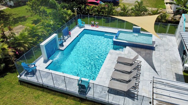 Ein rechteckiger Pool mit einer gefliesten Kante, umgeben von einer Glasumrandung. Liegestühle und ein kleines Spielbereich mit einer Rutsche sind vorhanden.