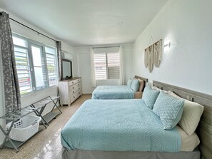 Ein Schlafzimmer mit zwei Betten, einem Schminktisch, einem Spiegel und einem Fenster mit Jalousien.