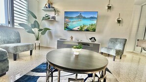 Una sala de estar moderna con una mesa redonda, dos sofás grises, un televisor plano grande y una planta decorativa.