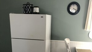A compact kitchen with a white refrigerator, a wooden dining table, and a wall clock. - Farm stay close to Colorado Springs! Pine trees, fresh air, goats and chickens! (Calhan)