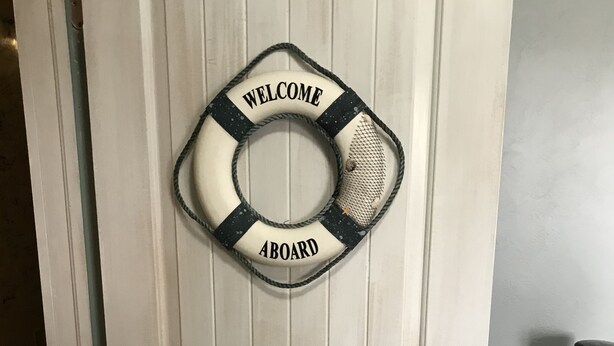 A white door with a life preserver sign reading "WELCOME ABOARD" and a metal handle. - Farm stay close to Colorado Springs! Pine trees, fresh air, goats and chickens! (Calhan)