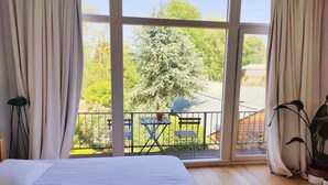A bedroom with a large window, a bed, a small table, and a potted plant. - Traditional chic high ceilings apt w Aircos/Garage (Antwerpen)