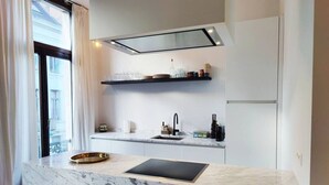 A modern kitchen with a marble countertop, a black induction cooktop, a stainless steel sink, and a black range hood. - Traditional chic high ceilings apt w Aircos/Garage (Antwerpen)