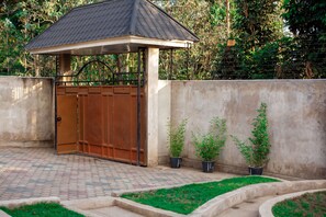 Une entrée fermée par un portail en métal, un mur en béton et des plantes en pot.