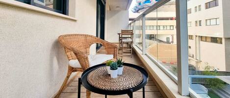 A balcony with wicker chairs, a small table with potted plants, and a view of buildings.