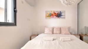 Ein Schlafzimmer mit einem Bett, zwei Nachttischen, einem Wandbild im abstrakten Stil und einem Spiegel.