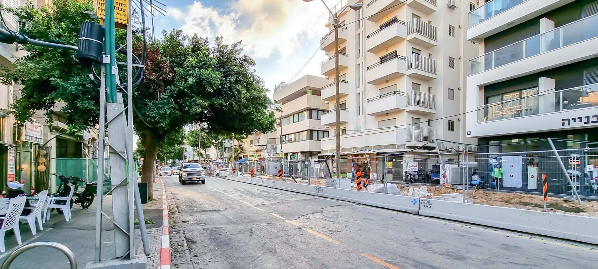 A street with a sidewalk cafe, a building under construction, and a parked car.