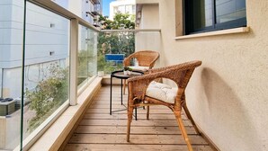 Ein Balkon mit Korbstühlen und einem kleinen Tisch, mit Blick auf eine Stadtlandschaft.