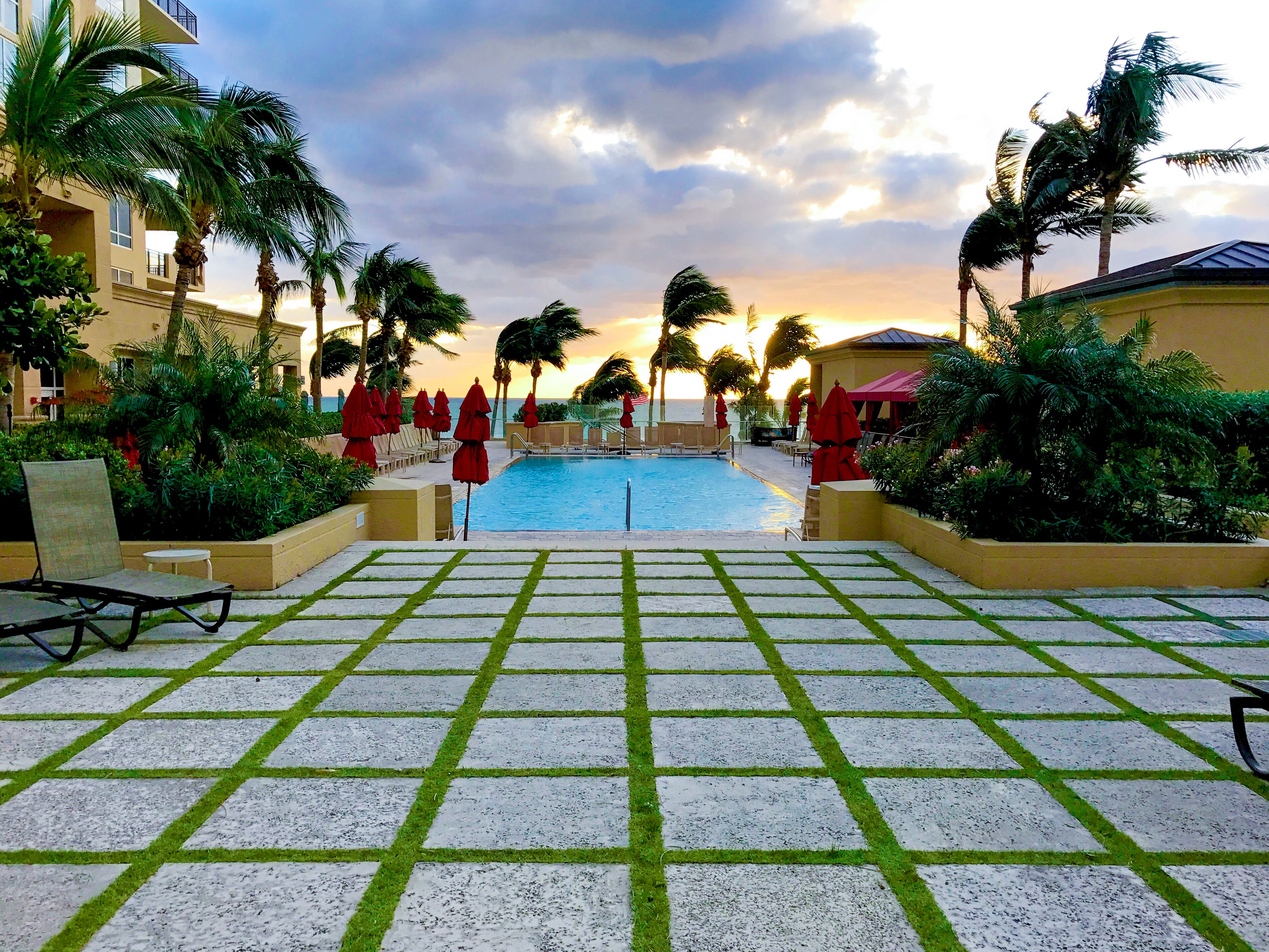 Un área de piscina con cubierta de baldosas, sillones de descanso y sombrillas.