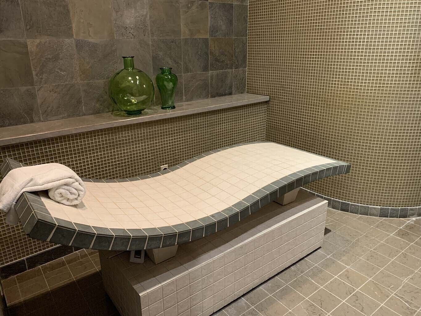 Une salle de bain avec un lavabo incurvé, une serviette posée sur le comptoir et une étagère ornée de deux vases verts.