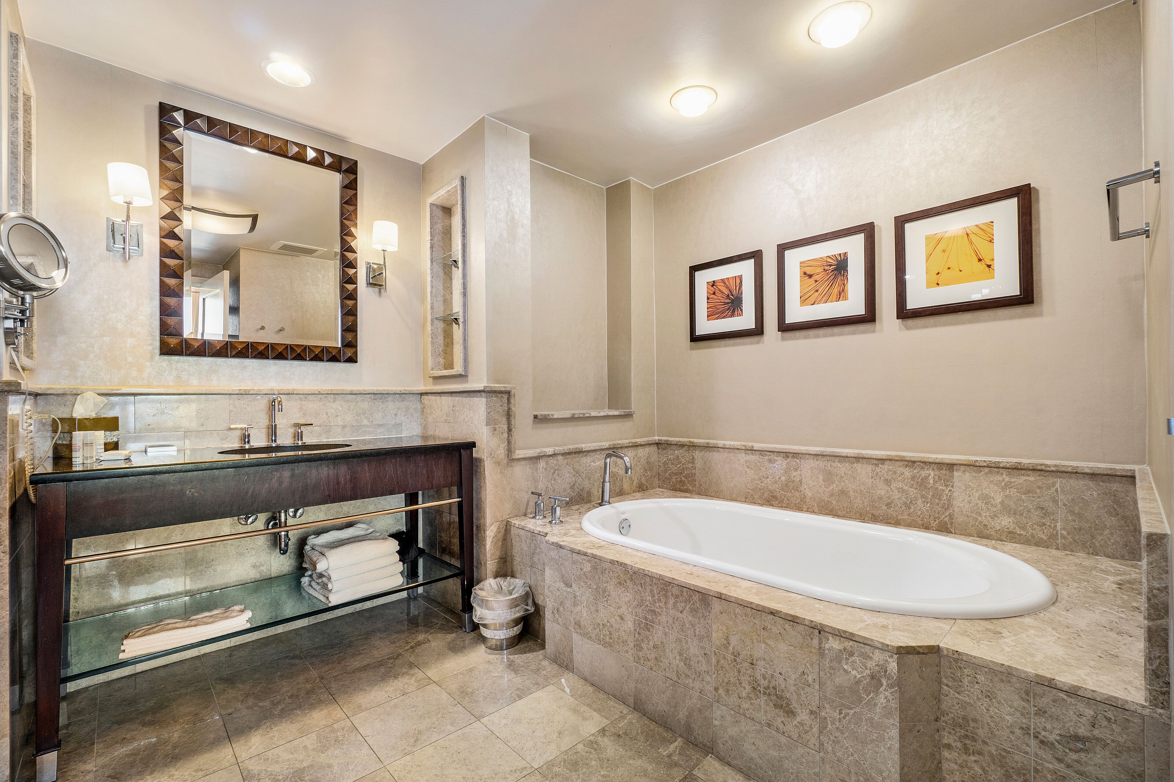 A modern bathroom with a large bathtub, a vanity with a mirror, and three framed pictures on the wall.