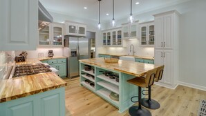 A modern kitchen with light blue cabinets, wooden countertops, and a central island with bar stools. - Luxury Lakefront Retreat w/ Deck & Patio! (Edgemont)