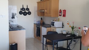 A compact kitchen with wooden cabinets, a microwave, and a dining area with a table and chairs. - Studio/scenic Views/pool/air Con/near Attractions (Pegeia)