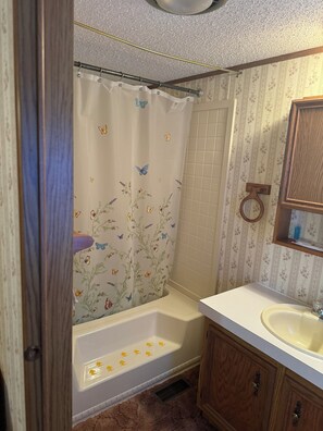 A bathroom with a shower curtain featuring butterfly designs, a bathtub, a sink, and wooden cabinets.