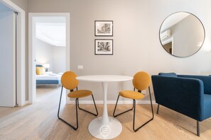 Un salon moderne avec une table ronde blanche, deux fauteuils de couleur moutarde, un canapé bleu et deux photographies en noir et blanc encadrées accrochées au mur.