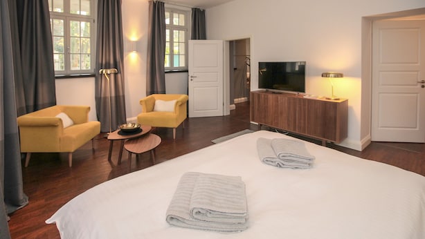 Una habitación de hotel con una cama grande, dos sillones, un televisor y un aparador de madera.