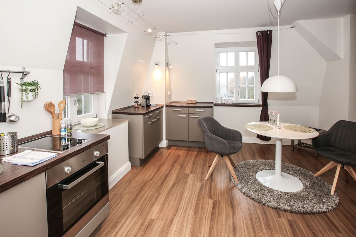 Cocina compacta con electrodomésticos modernos, comedor con mesa redonda y vista al exterior a través de una ventana.