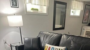 Ein schwarzes Ledersofa mit einem 'HAPPY'-Kissen, einer Stehlampe und einem Spiegel an der Wand.