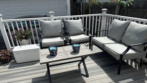 Eine Terrasse mit weißer Reling, zwei beigefarbene Polsterstühle, einem kleinen Tisch und zwei blauen Dekopflanzen.