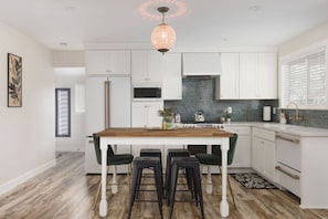 A modern kitchen with white cabinetry, a wooden island with bar stools, a gas stove, and a decorative pendant light.