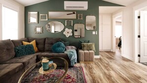 A living room with a dark green accent wall, a brown sofa, and a coffee table with a book and a mug. - Charming Home Downtown Paso+ Sleeps 6+Walkable+BBQ (Paso Robles)