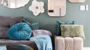 A living room with a grey sofa, teal and purple cushions, a white decorative flower, and a beige ottoman. - Charming Home Downtown Paso+ Sleeps 6+Walkable+BBQ (Paso Robles)