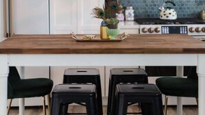 A kitchen with white cabinets, a wooden island with stools, a peacock decoration, and a hanging light fixture. - Charming Home Downtown Paso+ Sleeps 6+Walkable+BBQ (Paso Robles)
