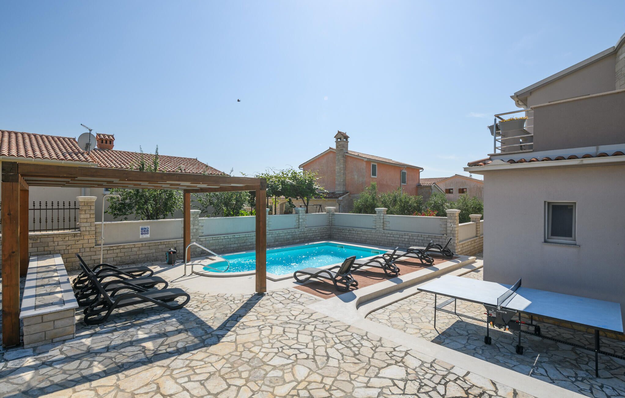 Une piscine avec des chaises longues, une pergola et une table équipée d’un barbecue.