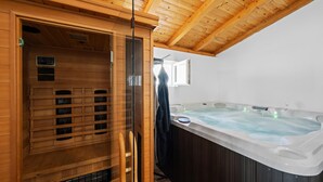 Una sala de sauna con interior de madera, puerta de vidrio y un jacuzzi con chorros.
