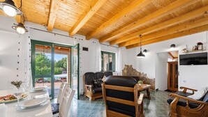 Una habitación amplia con un alto techo de madera, un área de comedor con una mesa dispuesta para dos personas y un rincón de descanso con dos sillas.