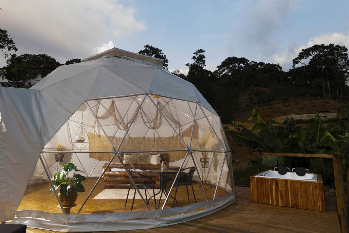 A geodesic dome structure with a wooden deck, a seating area, and a wooden bench with a sink.