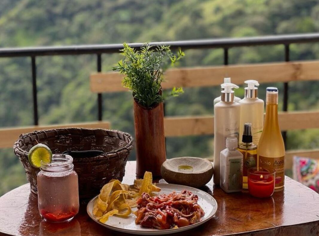 Una mesa con una bebida, aperitivos, una vela y artículos de tocador en un balcón con vistas a la vegetación.