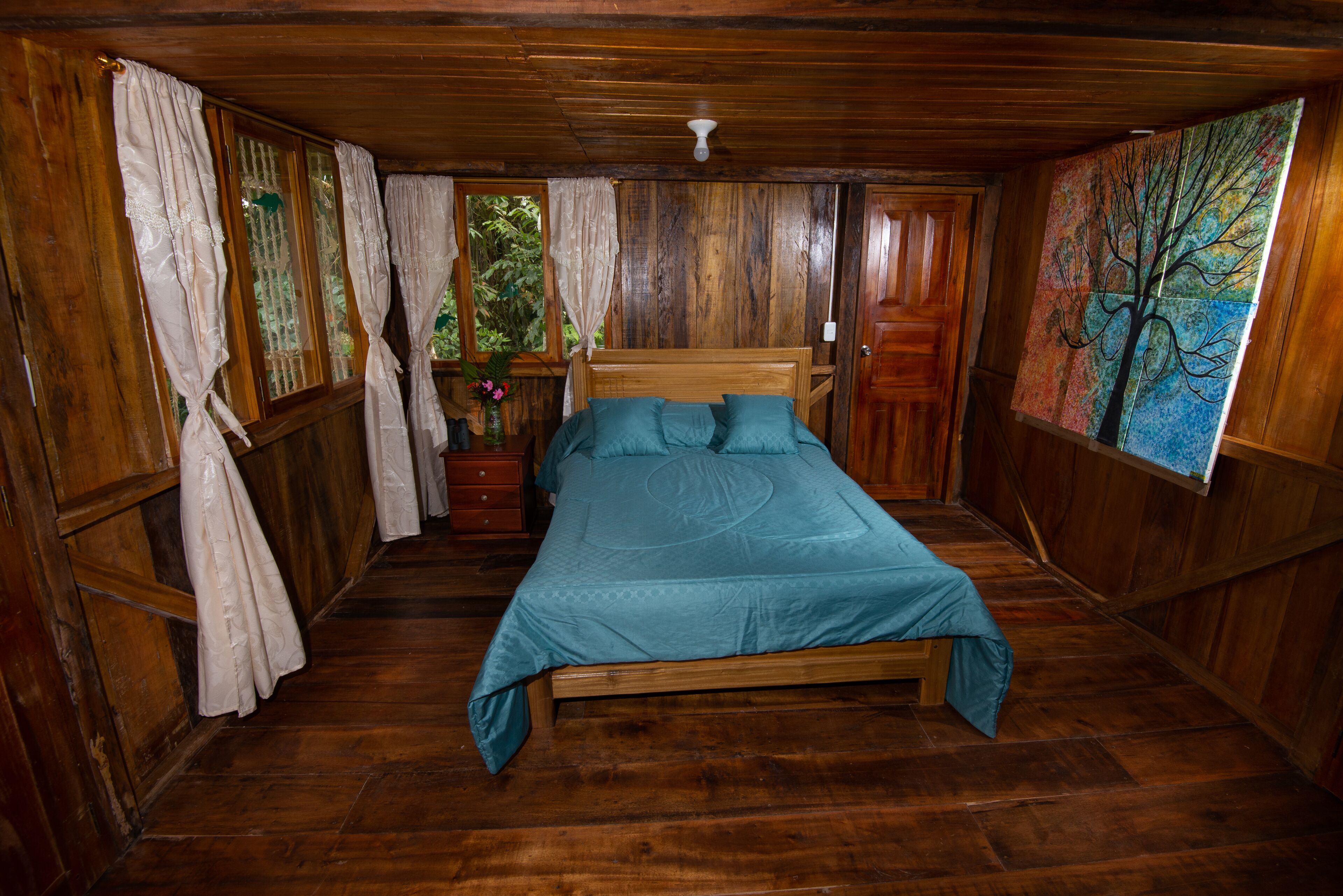 A wooden room with a bed, curtains, and a painting.