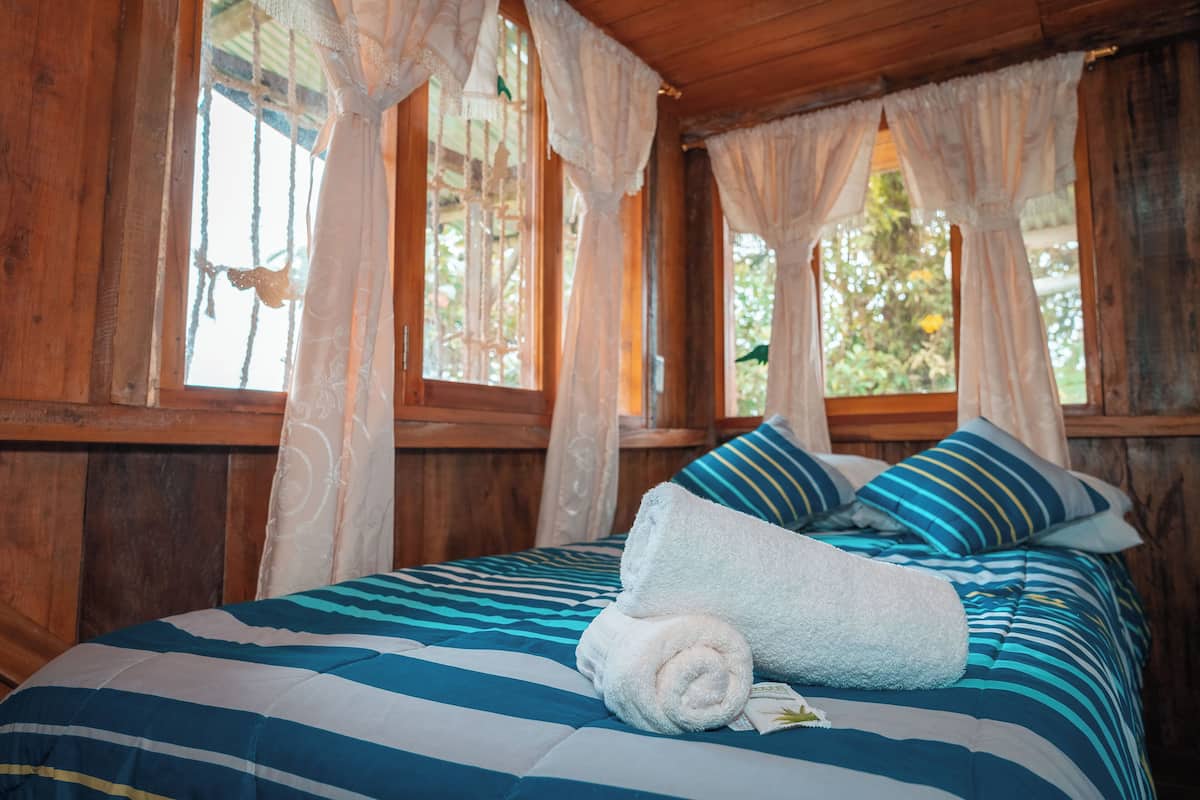 A wooden cabin bedroom with a bed, pillows, and a rolled towel.