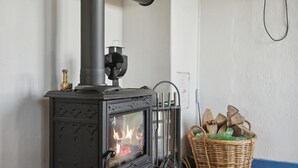 Ein Kaminofen mit Schornstein, in dem ein Feuer brennt, und ein Holzkorb daneben.