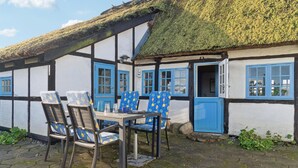Ein traditionelles Fachwerkhäuschen mit Strohdach, einem Holztisch mit Stühlen und einer blauen Tür.