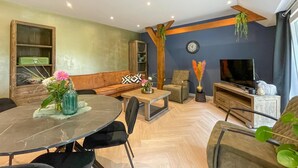 A modern living room with a sofa, coffee table, TV, and a dining area with chairs and a glass table. - Lovely home in Putten with kitchen (Putten)