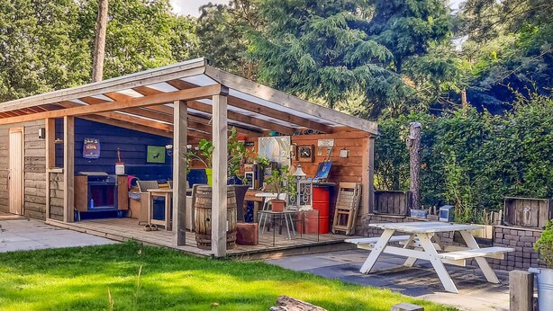 A wooden structure with a covered patio area, a barbecue setup, and various items on display. - Gorgeous home in Sint-Oedenrode (Sint-Oedenrode)