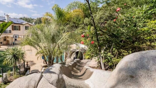 A stone sculpture in a garden with palm trees and red flowers. - Vacation house with spa, pool, and water slide. (El Cajon)