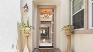 A hallway with a door leading to a room, flanked by two large potted plants. - Vacation house with spa, pool, and water slide. (El Cajon)