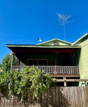 Una casa de dos pisos con un balcón, una antena parabólica y una valla de madera al frente.