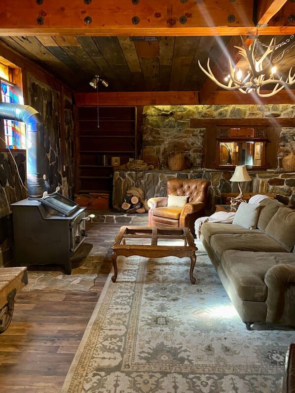 Una sala de estar acogedora con chimenea de piedra, techo de madera y un candelabro.