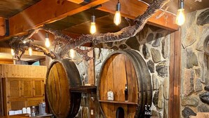 Eine rustikale Bar mit Holzfässern, einer Steinwand und einer Holztheke. Es gibt Hocker und einen Barhocker.
