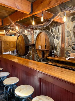 Un coin bar rustique avec des tonneaux en bois, un mur en pierre et un comptoir en bois. On y trouve des tabourets et un tabouret de bar.