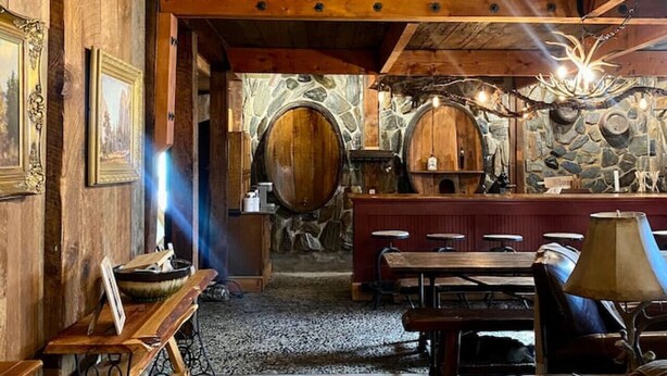 Ein rustikales Interieur mit Holzbalken, Steinwänden und einer Bar mit Hockern und einer Lampe.