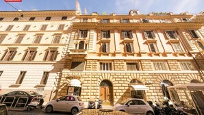 Un edificio histórico con múltiples ventanas y balcones, coches estacionados y un cielo despejado.